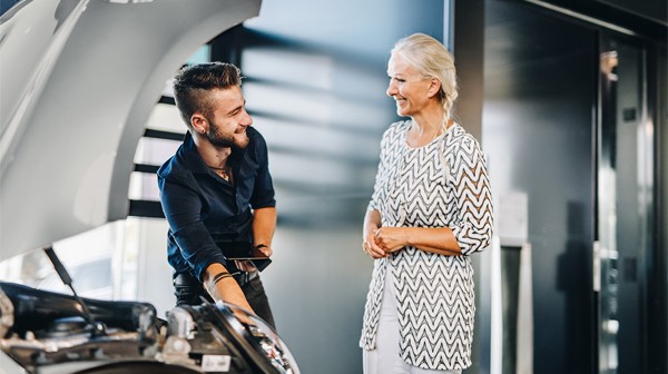 Ein Mann zeigt einer Frau etwas im Motorraum eines Autos mit geöffnetem Kofferraum.