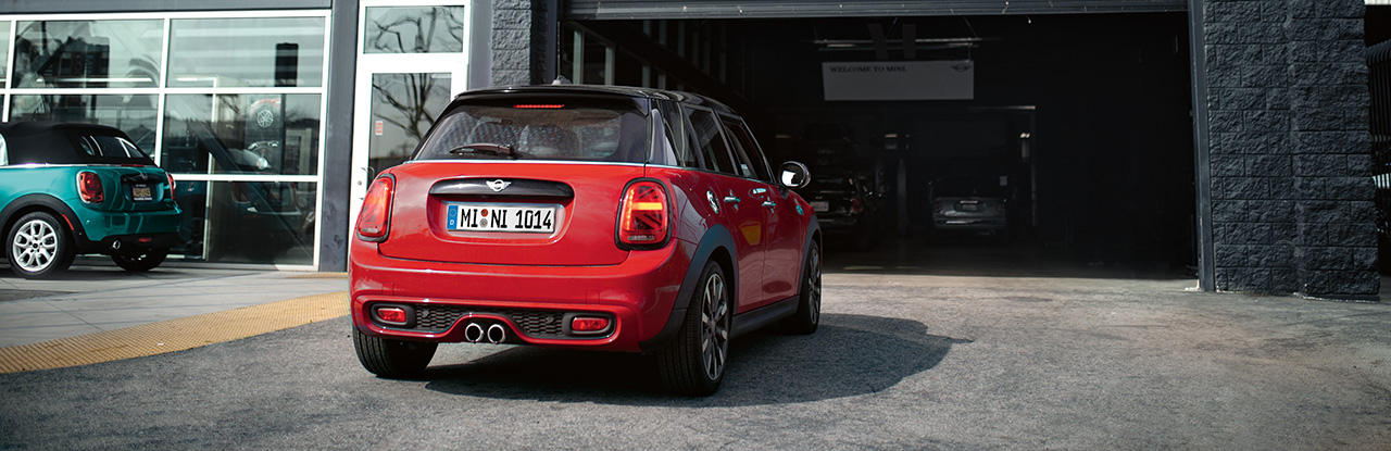 Roter MINI Cooper auf Parkplatz vor Werkstatt, im Hintergrund ein weiterer MINI.