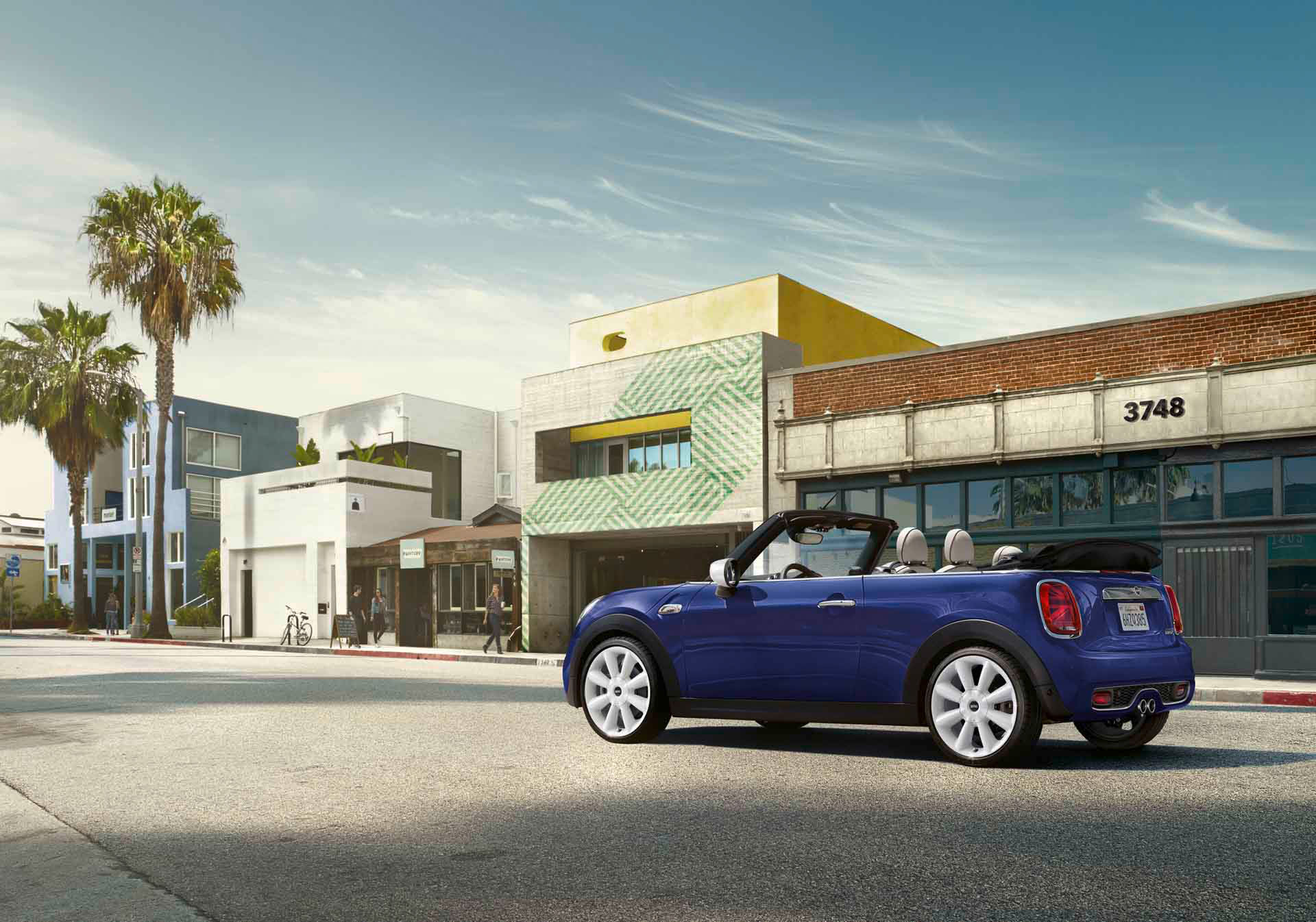 Blaues Cabrio auf Straße vor modernen Gebäuden und Palmen, sonniger Tag.