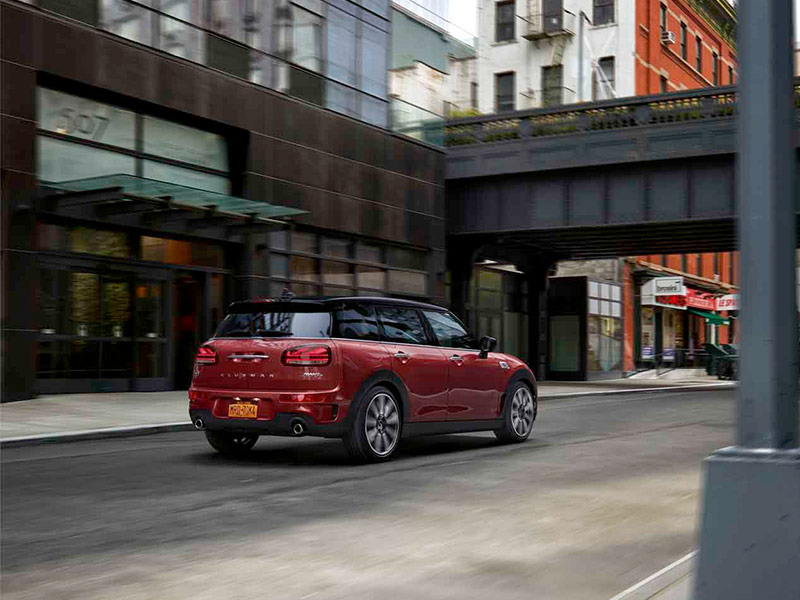 Roter MINI Clubman fährt durch eine Stadt, umgeben von modernen Gebäuden und einer Brücke.