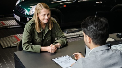 Eine Frau im Gespräch mit einem Mann am Schreibtisch, im Hintergrund ein grüner MINI.