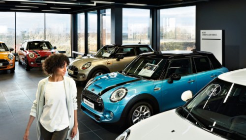 Frau in einem Autohaus mit mehreren ausgestellten MINI-Fahrzeugen in verschiedenen Farben.