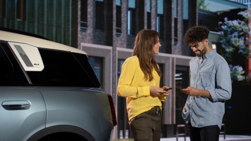 Eine Frau und ein Mann stehen neben einem blauen Auto und schauen auf ihre Smartphones.