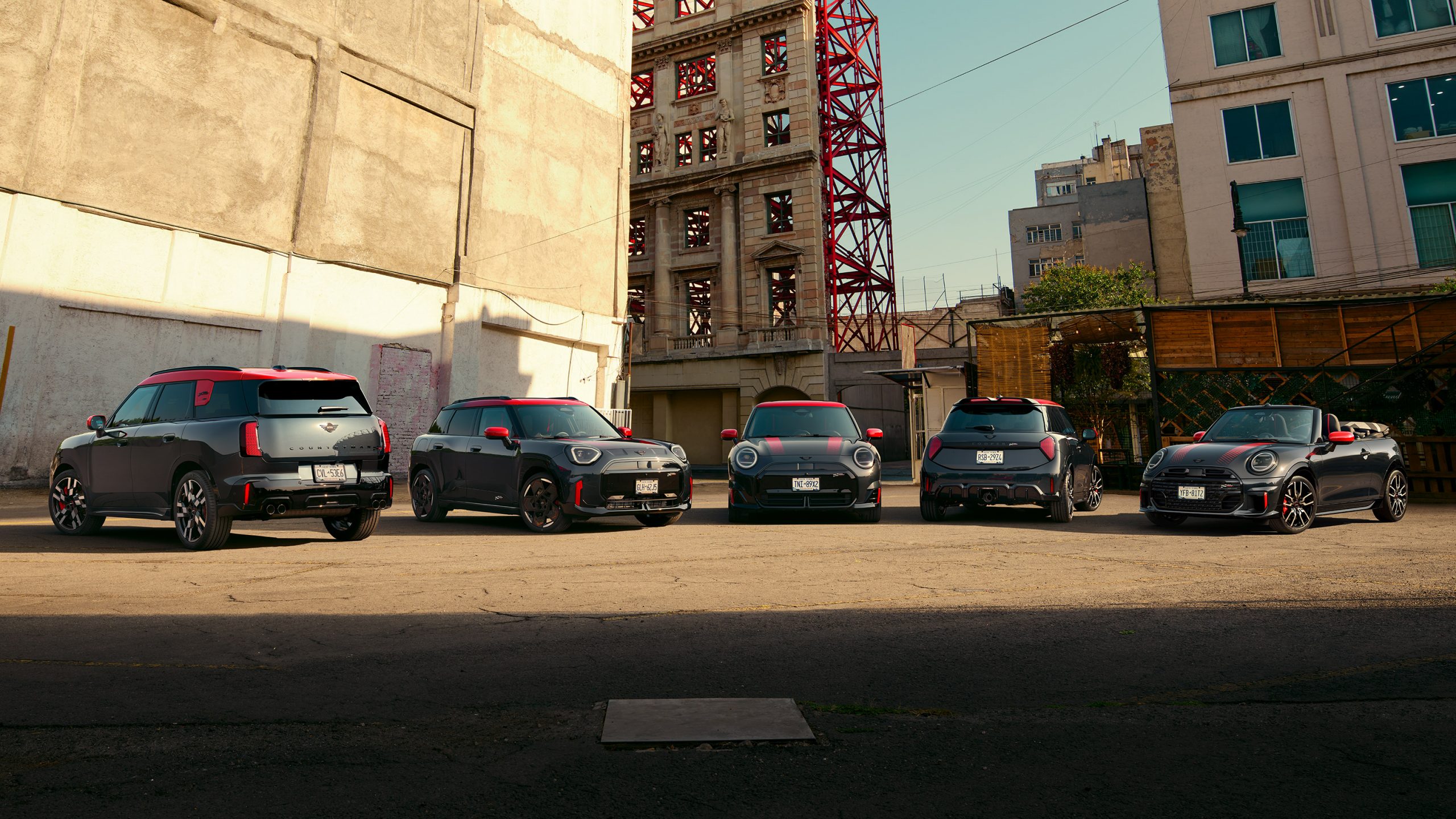 Fünf schwarze und rote MINI-Cooper vor urbaner Kulisse bei Tageslicht.
