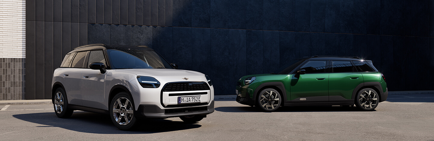 Zwei MINI-Autos, ein weißes und ein grünes, stehen auf einem Parkplatz vor einer dunklen Wand.