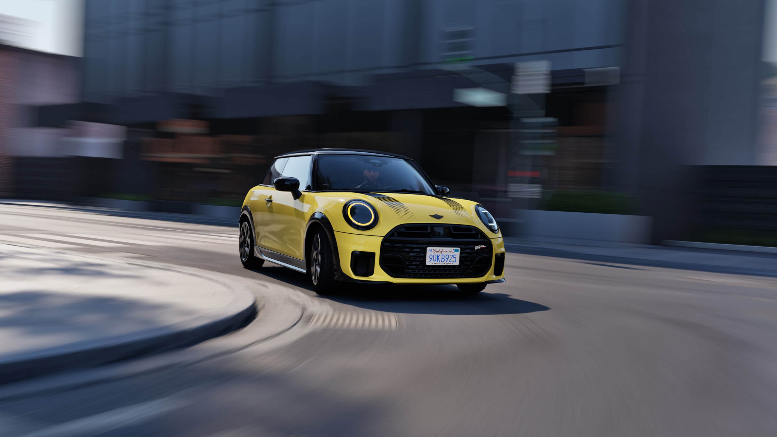 Gelber MINI Cooper fährt dynamisch durch eine Stadtstraße, unscharfer Hintergrund.