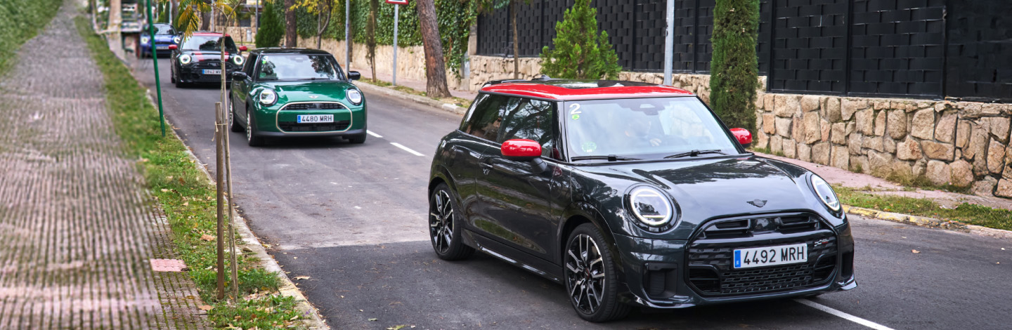 Mehrere MINI Cooper fahren auf einer Straße entlang einer Steinmauer.