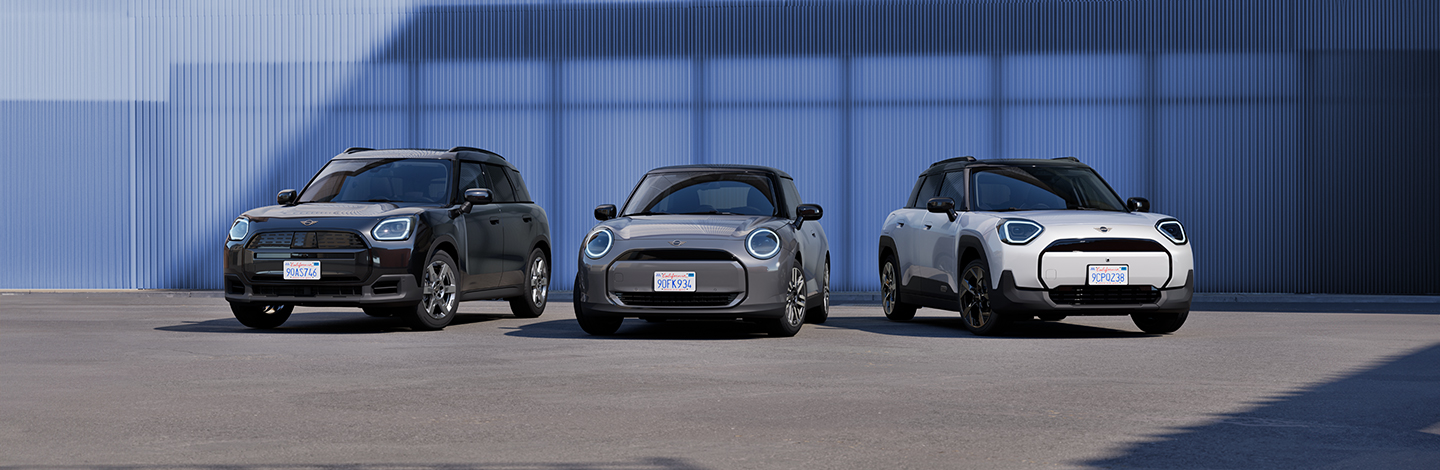 Drei MINI-Autos in verschiedenen Farben stehen nebeneinander vor einer blauen Metallwand.