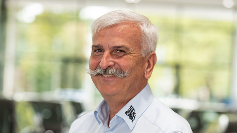 Älterer Mann mit weißem Haar und Schnurrbart lächelt in einem hellen Raum.