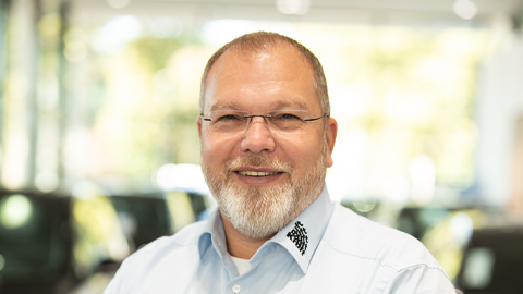 Ein Mann mit Brille lächelt in die Kamera. Er trägt ein helles Hemd.