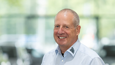 Mann in hellem Hemd lächelt vor unscharfem Hintergrund.