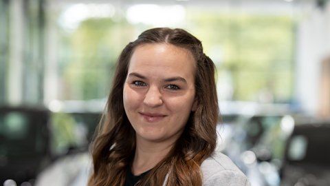 Eine Frau lächelt in die Kamera, Hintergrund unscharf mit Autos.