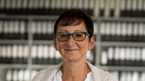 Frau mit Brille vor Regalen voller Ordner, lächelt. Hintergrund unscharf.