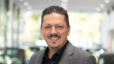 Ein lächelnder Mann in Anzug posiert in einem modernen, hellen Autohaus.