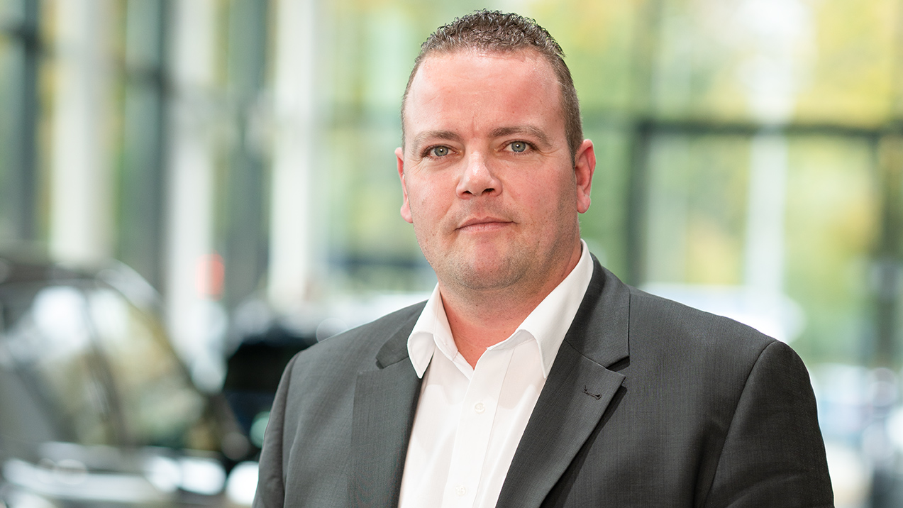 Mann im Anzug vor unscharfem Hintergrund in einem Autohaus.