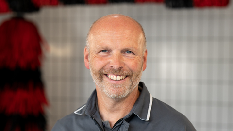 Ein lächelnder Mann vor einer Kachelwand in einer Werkstattumgebung.