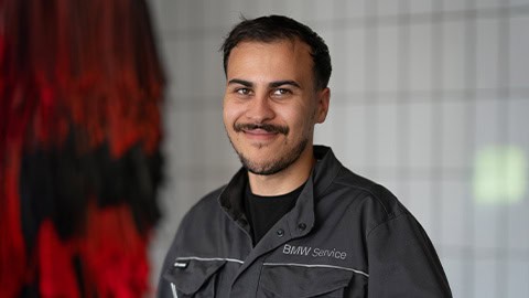 Ein Mann in BMW-Service-Uniform lächelt in die Kamera, Hintergrund unscharf.
